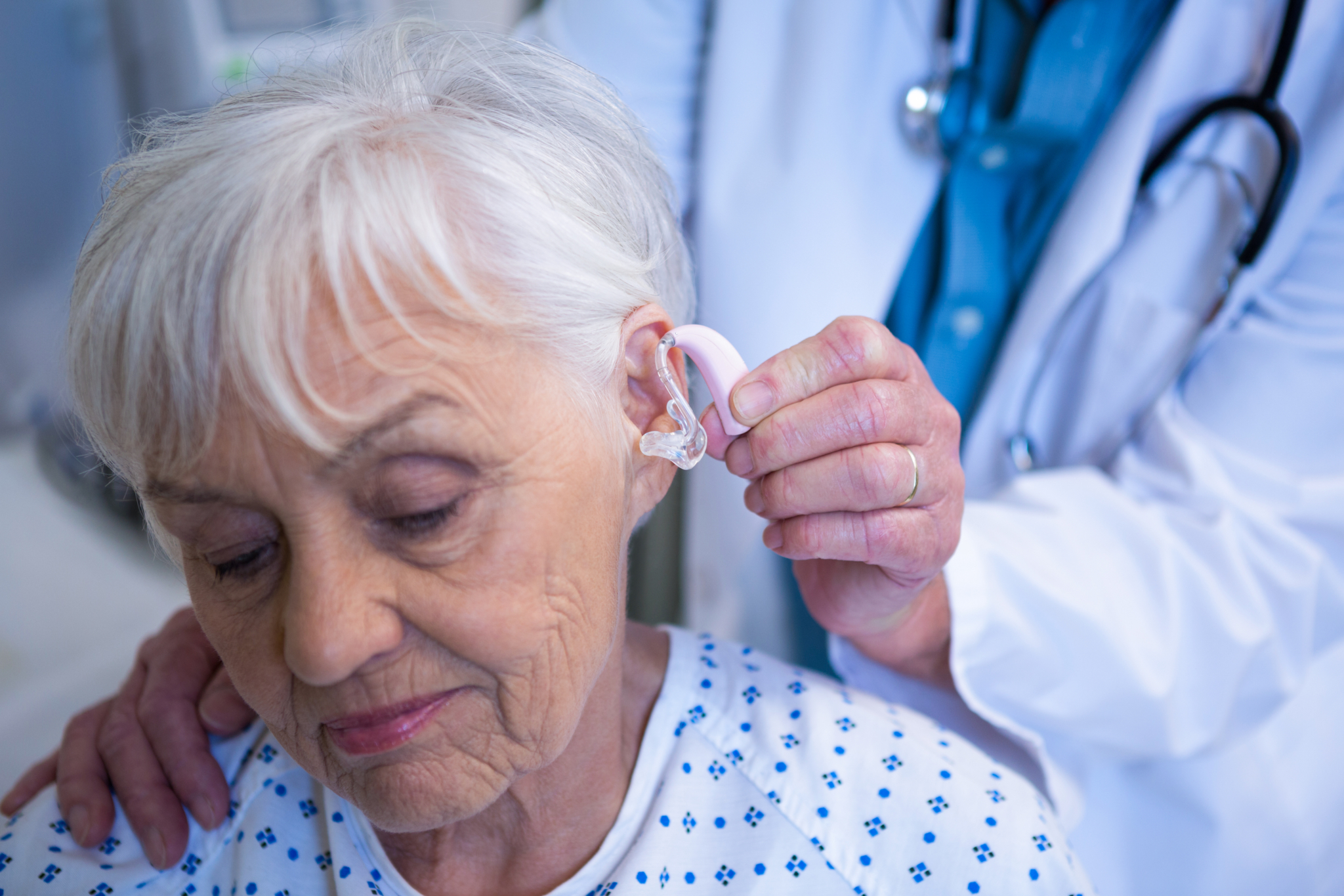 Doctor inserting hearing aid in senior patient ear Audiomédica
